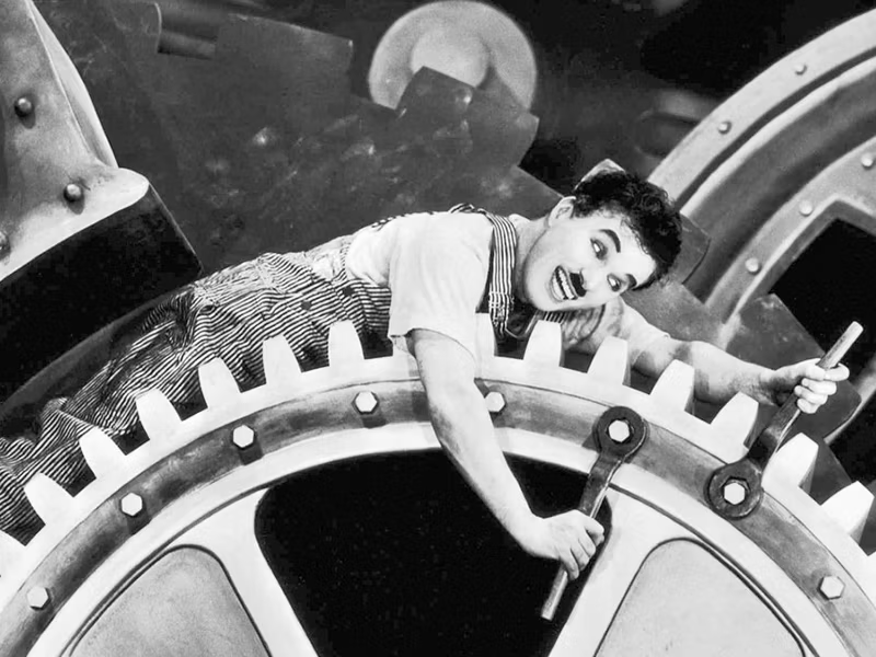 Esta imagem marcante retrata o icônico ator e diretor Charles Chaplin no aclamado filme "Tempos Modernos" (Modern Times), lançado originalmente no ano de 1936.